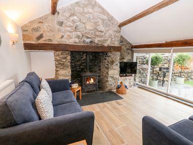 A living room with a stone fireplace a wood burning stove blue sofas and large windows at Y Bwthyn in Dyffryn Ardudwy