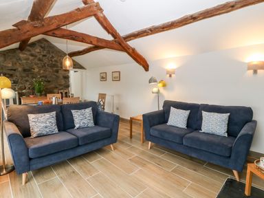 A living room with two blue sofas and wooden beams at Y Bwthyn in Dyffryn Ardudwy