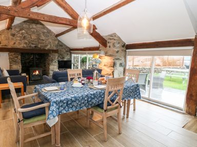 A dining area with wooden chairs and a blue tablecloth in a room with exposed wooden beams and a stone fireplace at Y Bwthyn in Dyffryn Ardudwy