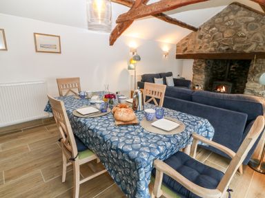 A dining table with bread and cups in a living room with blue sofas and a stone fireplace at Y Bwthyn in Dyffryn Ardudwy