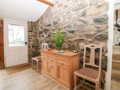 A hallway with a wooden sideboard and two chairs against a stone wall at Y Bwthyn in Dyffryn Ardudwy