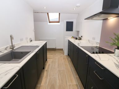 A kitchen with dark cabinets white marble countertops a sink stovetop and a skylight at Y Bwthyn in Dyffryn Ardudwy