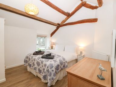 A bedroom with a double bed beside a window and wooden beams on the ceiling at Y Bwthyn in Dyffryn Ardudwy