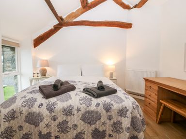 A bedroom with a bed table lamps a desk and visible wooden ceiling beams at Y Bwthyn in Dyffryn Ardudwy