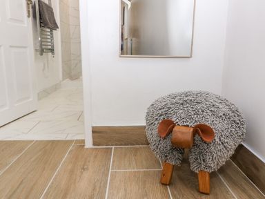 A small gray sheep-shaped stool next to a mirror on a wood floor at Y Bwthyn in Dyffryn Ardudwy
