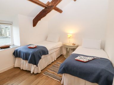 A bedroom with two single beds a small round table with a lamp between the beds and a window on the left at Y Bwthyn in Dyffryn Ardudwy