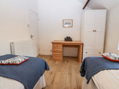 A bedroom with two single beds blue blankets a wooden desk white wardrobe and a radiator at Y Bwthyn in Dyffryn Ardudwy