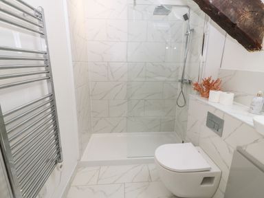 A bathroom with a wall-mounted toilet shower area with glass door towel rack and decorative items on a shelf at Y Bwthyn in Dyffryn Ardudwy