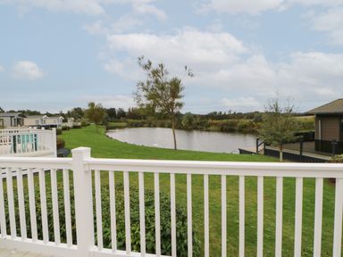 A view of a pond with grass and trees from a white balcony railing at 10 Cheviot View in Haggerston near Lowick