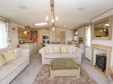 An open plan living room and kitchen with beige sofas and a green ottoman at 10 Cheviot View in Haggerston near Lowick