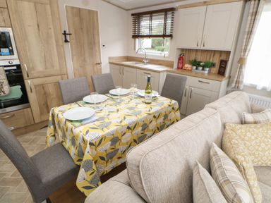 A dining area with a table set for four next to a kitchen and a sofa at 10 Cheviot View Haggerston near Lowick