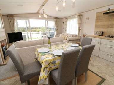 A dining area with a table set for four and a living room with sofas and a television in the background at 10 Cheviot View in Haggerston near Lowick