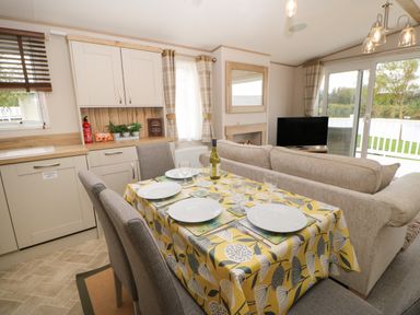 A dining area with a table set for four next to a kitchen and beige sofa in a living room at 10 Cheviot View Haggerston near Lowick