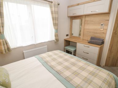 A bedroom with a bed covered with a plaid blanket a dressing table with a mirror and a stool and folded towels on top at 10 Cheviot View in Haggerston near Lowick
