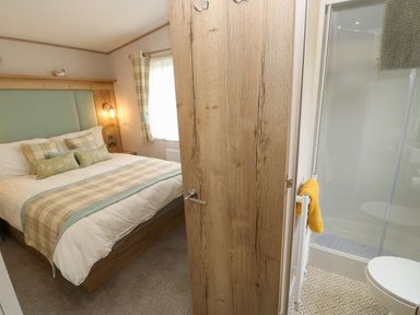 A bedroom with a bed and plaid curtains next to a bathroom with a shower at 10 Cheviot View in Haggerston near Lowick