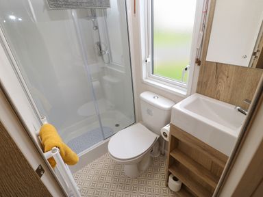 A small bathroom with a shower, toilet, sink, and a window at 10 Cheviot View in Haggerston near Lowick