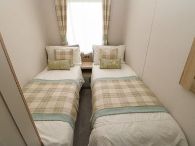 A bedroom with two single beds with plaid blankets and pillows separated by a small wooden nightstand at 10 Cheviot View in Haggerston near Lowick