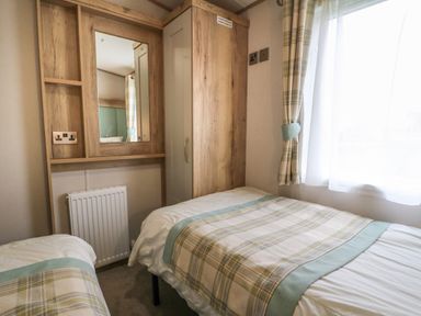 A bedroom with two single beds, wardrobe with mirror, radiator, and window with curtains at 10 Cheviot View in Haggerston near Lowick