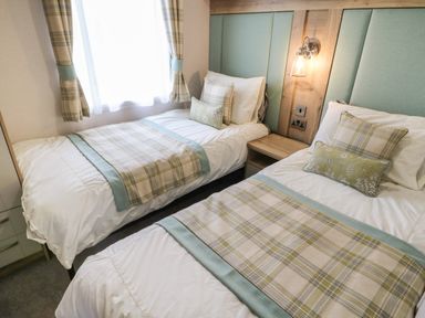 A twin bedroom with plaid bedding and pillows two beds a window and a nightstand at 10 Cheviot View in Haggerston near Lowick