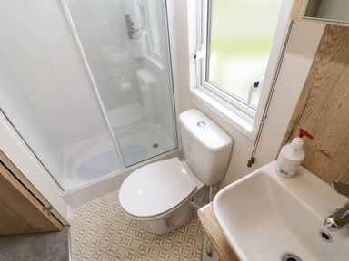 A bathroom with a shower, toilet, sink, and window at 10 Cheviot View in Haggerston near Lowick