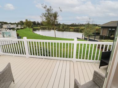 A view of a lake and grassy area from a balcony with white railing and outdoor chairs at 10 Cheviot View in Haggerston near Lowick