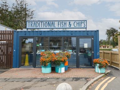 A traditional fish and chips shop with glass doors and flower pots outside in blue barrels