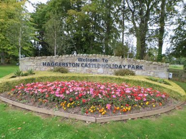 A flower bed with multi colored flowers in front of a stone sign that reads welcome to Haggerston Castle Holiday Park in Haggerston near Lowick