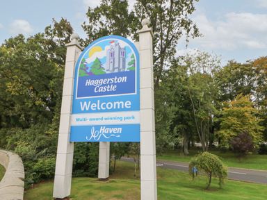 A welcome sign for Haggerston Castle multi award winning park with trees and a road in the background at 10 Cheviot View in Haggerston near Lowick