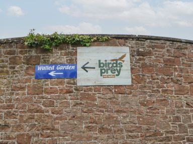 A stone wall with two signs pointing left to walled garden and birds of prey and reptiles at 10 Cheviot View in Haggerston near Lowick