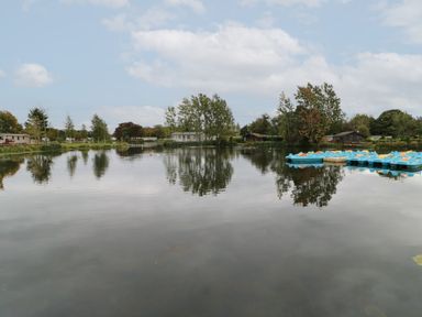 A lake with blue paddle boats and trees reflected in the water at 10 Cheviot View in Haggerston near Lowick