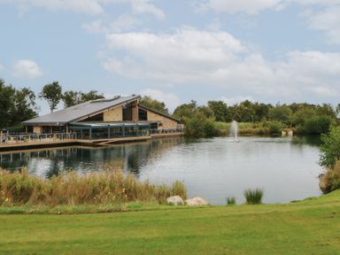 A building with outdoor seating next to a pond with a fountain and grassy area at 10 Cheviot View in Haggerston near Lowick