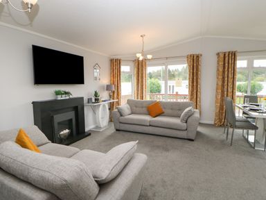 A living room with two gray sofas orange cushions a black fireplace a wall-mounted TV and a dining table by windows with orange curtains at Mildred's Lodge in Felton