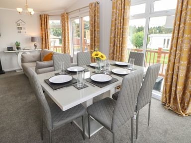 A dining table with six chairs set with plates and glasses in a room with yellow patterned curtains and a gray sofa at Mildred's Lodge in Felton