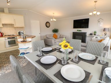 A dining table set with plates and glasses next to a kitchen and living area with sofas and a wall-mounted TV at Mildred's Lodge in Felton