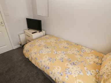 A single bed with yellow floral bedding next to a white bedside table with a television on top at Mildred's Lodge in Felton