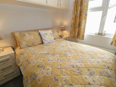 A bedroom with a bed covered in yellow floral bedding two bedside tables with lamps and a window with matching curtains at Mildred's Lodge in Felton