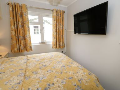 A bedroom with a bed covered by a yellow floral bedspread a window with yellow floral curtains and a wall-mounted television at Mildred's Lodge in Felton