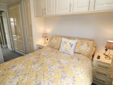 A bedroom with a bed covered in yellow floral bedding two bedside tables with lamps and built-in cabinets at Mildred's Lodge in Felton