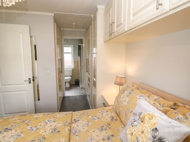 A bedroom with yellow floral bedding a bedside table with lamp built in wardrobes and an ensuite bathroom at Mildred's Lodge in Felton