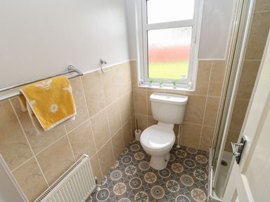 A small bathroom with a toilet a shower cubicle a towel rail with yellow towel and patterned floor at Mildred's Lodge in Felton