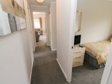 A hallway with carpet leading to a living room and a bedroom with a bed and a television on a cabinet at Mildred's Lodge in Felton