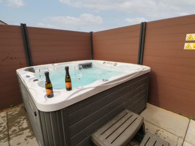 An outdoor hot tub with water and two bottles with two glasses on the edge surrounded by brown fencing at Mildred's Lodge in Felton