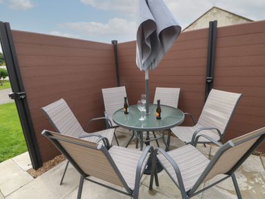 An outdoor seating area with six chairs around a glass table and a closed umbrella at Mildred's Lodge in Felton
