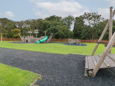 An outdoor playground with a wooden ship structure slide and climbing frame on grass surrounded by trees