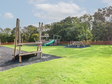 An outdoor playground with wooden climbing structures and a green slide on a grassy field surrounded by trees at Mildred's Lodge in Felton
