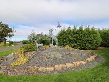 An outdoor garden area with two stag statues a flagpole and trees in the background at Mildred's Lodge in Felton