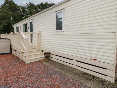 An exterior view of a beige mobile home with steps leading to a small porch and a gravel ground at Hedgehog Retreat in Felton