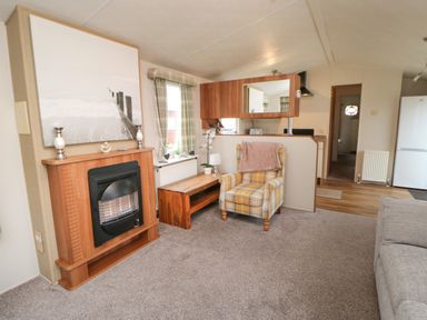 A living room with a fireplace a yellow plaid armchair a wooden bench and a kitchen area at Hedgehog Retreat in Felton