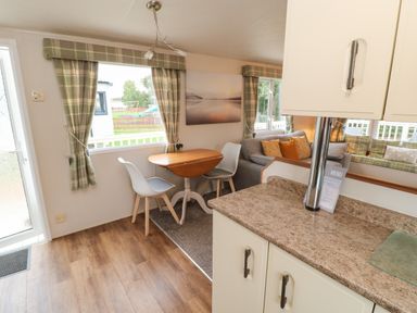 A dining area with a drop-leaf table and two chairs next to windows with plaid curtains and a kitchen counter in the foreground at Hedgehog Retreat in Felton