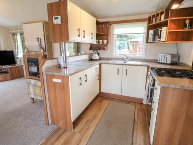 A kitchen with cupboards a stove a sink and a toaster next to a living room with a television and armchair at Hedgehog Retreat in Felton
